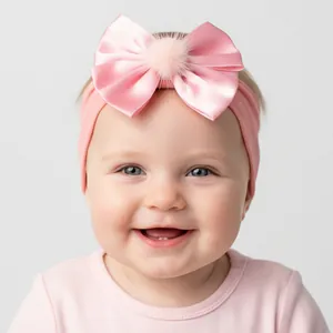 Detail of pink nylon baby headband with large satin bow and soft plush pom-pom decoration