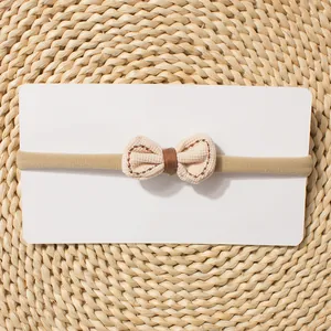 Detail of baby bow headband with beige fabric and brown stitching on woven mat