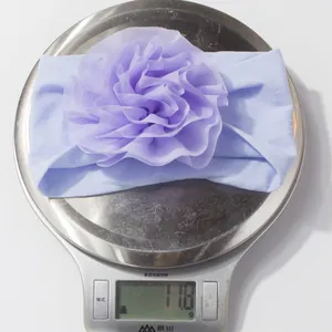 Détail du bandeau bébé violet avec fleur en résille pesant 11,8g sur une balance