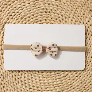 Detail of baby elastic headband with floral bow on display card with straw mat background