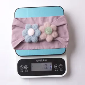 Detail shot of a purple nylon baby headband with floral accents on a digital scale