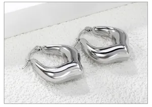 Macro view of polished silver U-shaped chunky earrings on white stone background
