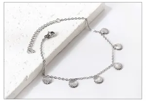Detail of silver shell pendant anklet with adjustable chain on textured stone
