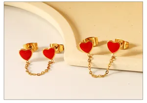 Detail van gouden ketting oorbellen met twee rode emaille harten voor dubbele gaatjes