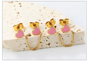 Close-up van roze hart emaille oorbellen met gouden ketting op natuursteen