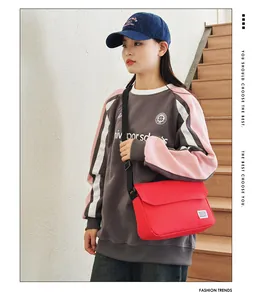 Detail of red messenger bag with adjustable black strap worn over a pink sweatshirt