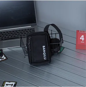 Close-up of minimalist black canvas phone bag with white logo on a modern workspace table