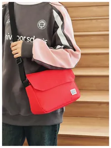 Red canvas messenger bag with adjustable strap shown worn on a casual hoodie