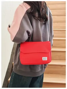 On-body view of a red canvas messenger bag with an adjustable black strap on stairs