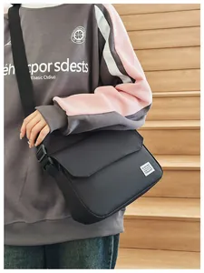 Close-up of black messenger bag with flap cover and white logo on casual sweatshirt