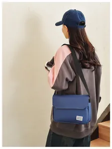 Dark blue canvas messenger bag with adjustable strap worn by a model on a light background