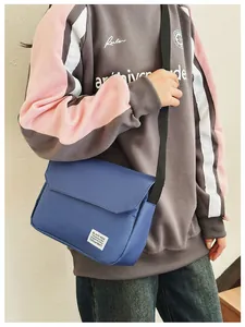 Detail of navy blue canvas messenger bag with brand label worn by model outdoors