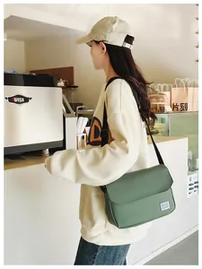 Dark green leather messenger bag with adjustable strap worn by model in cafe setting