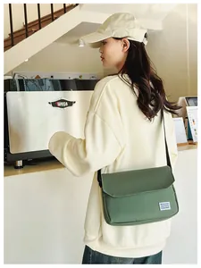 Army green canvas messenger bag with flip cover and woven label shown in casual cafe setting