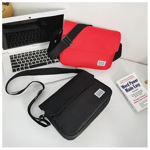 Flat lay of red and black canvas messenger bags with adjustable straps on a white desk