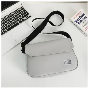 Close-up of light gray messenger bag with texture, flap closure and black shoulder strap