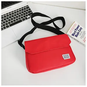 Detail of red canvas messenger bag showing a white fabric label and black nylon strap