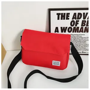 Close-up of red canvas messenger bag featuring a white brand label and black strap