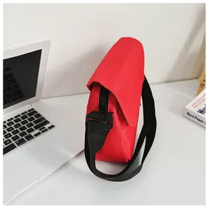 Detailed view of red canvas messenger bag with black adjustable strap on a white desk