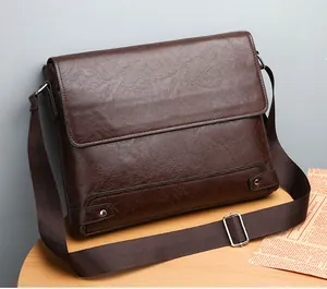 Detail of dark brown leather messenger bag with flap closure and silver buckle on wood desk