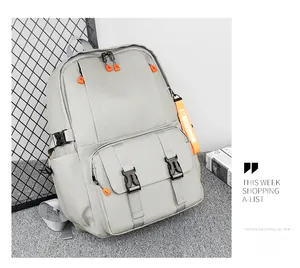 Close-up of light gray nylon backpack with double buckle closures and orange zipper detail