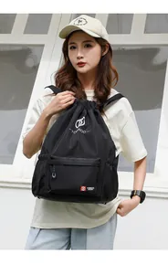 Detail of the black drawstring backpack featuring a white logo and side storage pocket
