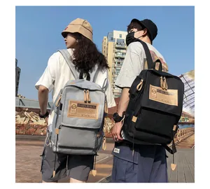 Front view of grey and black canvas backpacks showing retro woven labels and utility pockets