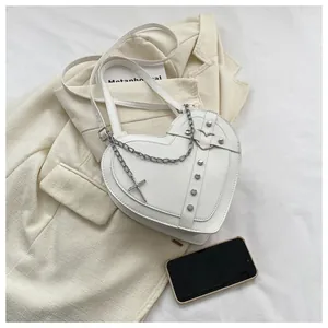 Detailed close-up of white heart-shaped handbag with silver studs and cross pendant