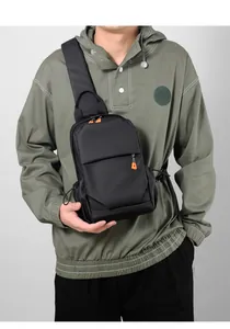 Detail of a black waterproof crossbody chest bag with orange zipper pullers on a male model