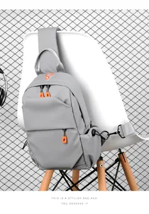 Close-up of gray nylon crossbody bag with orange zipper pull hanging on a white chair