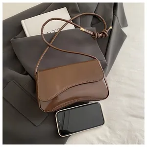 Detail of a brown patent leather crossbody bag with knotted strap and gold metal hardware