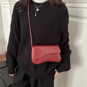 Glossy red asymmetrical crossbody bag in patent leather worn with black sweater