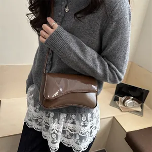 Brown glossy patent leather shoulder bag with asymmetrical curved flap design