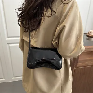 Modern black patent leather crossbody bag with wave flap design worn on a trench coat
