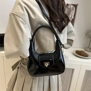 Minimalist black patent leather hobo bag with gold buckle shown on a model's shoulder