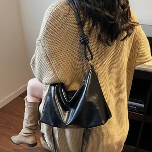 Sac bandoulière noir élégant avec sangle nouée et texture plissée porté par un mannequin