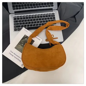 Détail macro du sac demi-lune en daim caramel avec bandoulière nouée sur un bureau