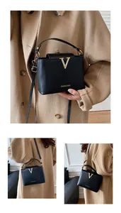 Λεπτομέρεια της μαύρης τετράγωνης τσάντας με χρυσή αγκράφα V και γράμματα μόδας
