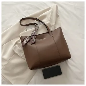 Détail du sac cabas en cuir marron avec logo doré et foulard décoratif en soie