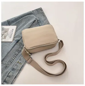 Detail view of a beige nylon crossbody bag with wide adjustable strap and zipper closure