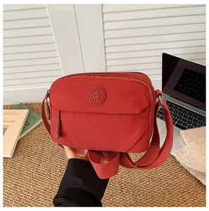 Detail of red nylon crossbody bag with adjustable wide strap and round logo branding