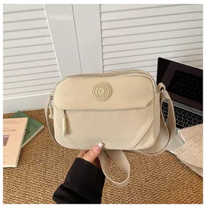 Detail of beige nylon crossbody bag featuring front zipper pockets and woven shoulder strap