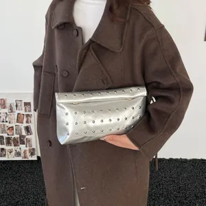 Silver metallic rivet clutch bag shown on a model wearing a brown wool coat