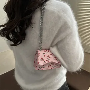 Pink cherry pattern crossbody bag with silver chain strap worn over white sweater