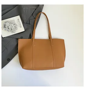 Close-up of brown matte leather tote bag with vertical stitching on a gray blazer background