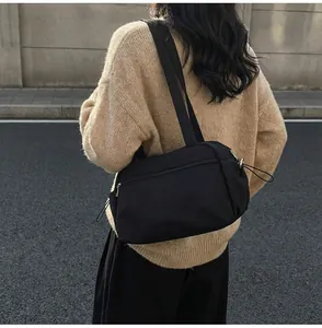 Detail of minimalist black nylon shoulder bag with drawstring sides on a street background