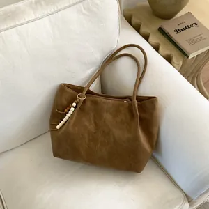 Brown faux suede tote bag with decorative wooden beads on a white sofa for daily commute
