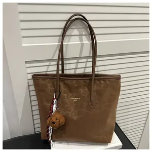 Detail of a brown leopard print tote bag with a plush dog charm and gold logo lettering