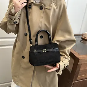 Grand sac cabas rétro en daim noir avec boucle dorée porté par un mannequin en trench kaki