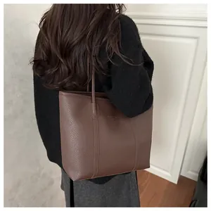 Detail view of large dark brown tote bag with lychee grain texture on a model's shoulder
